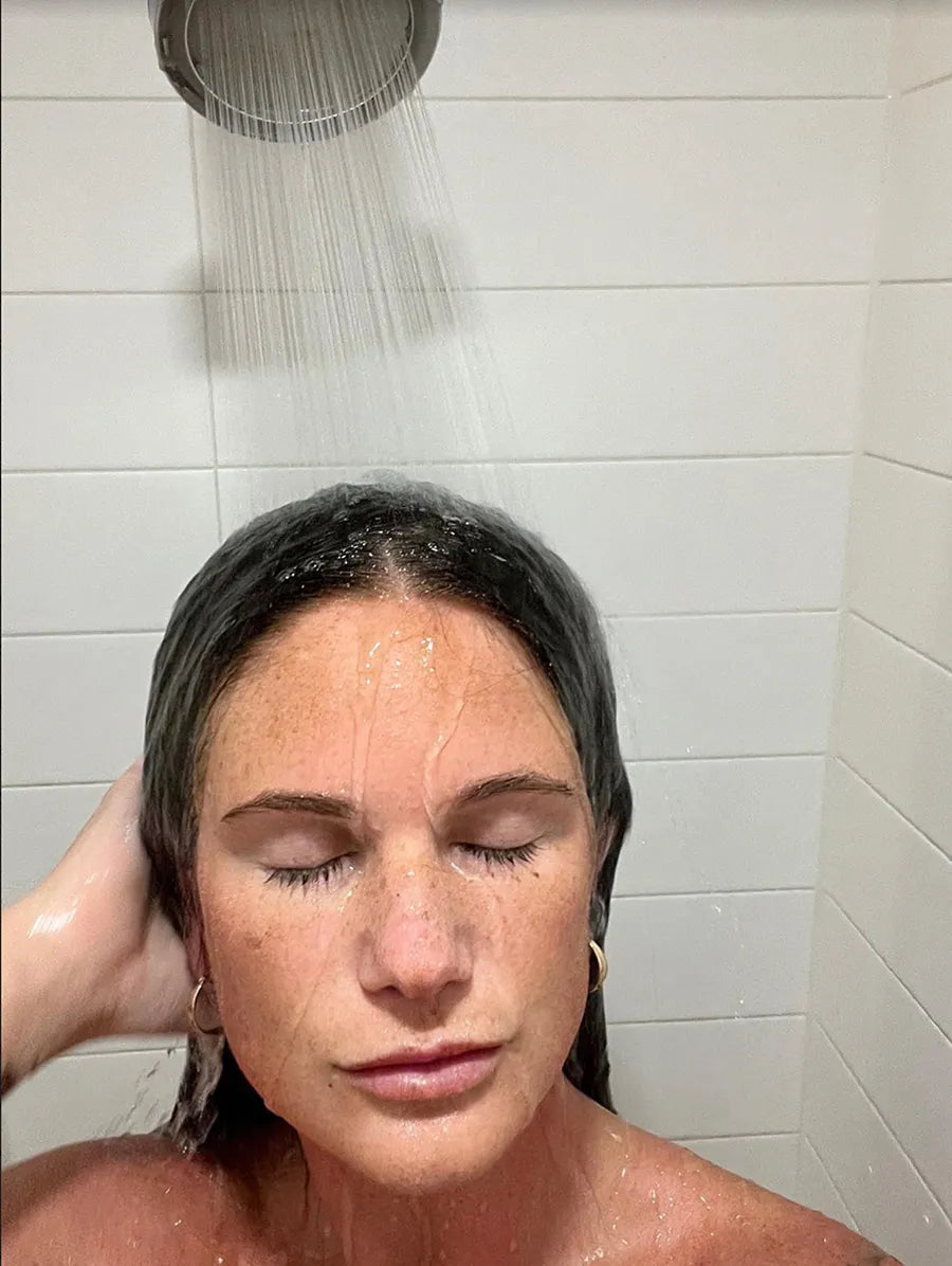 Person taking a shower with eyes closed, water flowing from showerhead.