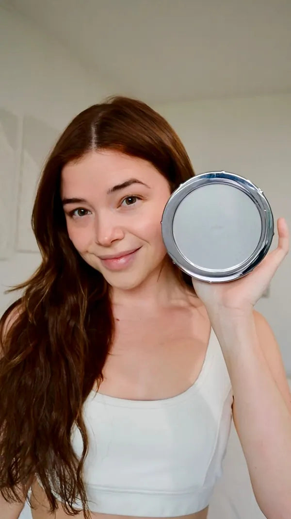 Woman holding a round silver object and smiling at the camera.