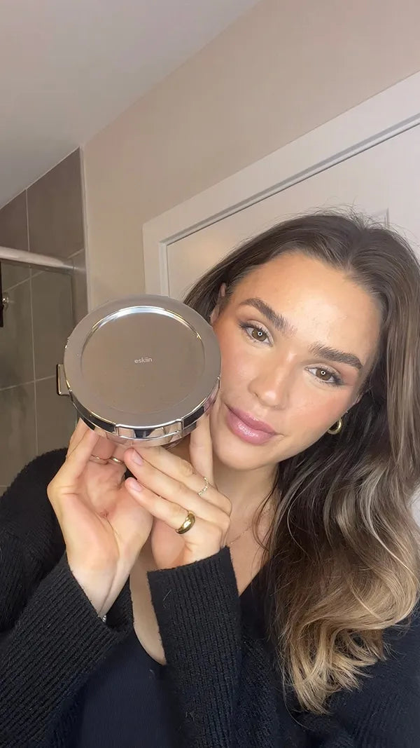 A woman holding a round metallic product container in a bathroom.