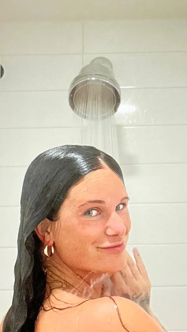 Person showering, looking back with a slight smile, water flowing from the showerhead.